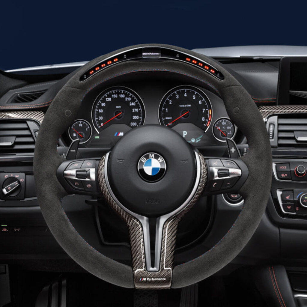 BMW M Performance Lenkrad 5 Nahaufnahme eines BMW M Performance Lenkrads mit Carbonfaser-Finish, analogen Tachometer