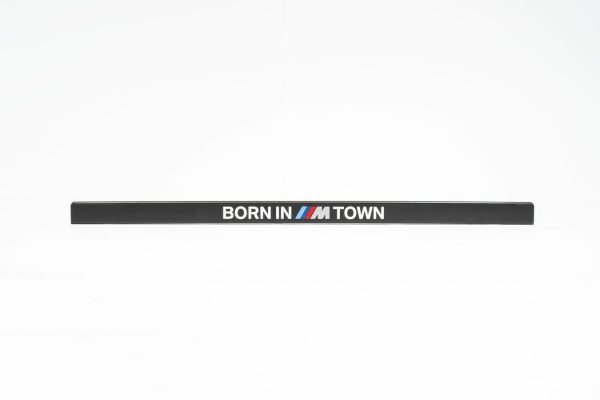 Der "kennzeichenhalter born in m town 3" ist ein schwarzer BMW Kennzeichenhalter mit dem Text BORN IN M TOWN, mit dem M in blauen, lila und roten BMW M Streifen, dargestellt auf einem schlichten weißen Hintergrund.